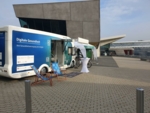 Der Digital Health Truck und der Pavillon der KTBW stehen bei gutem Wetter vor einem grauen Gebäude.